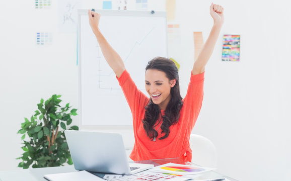 Excited woman raising her arms while working on her laptop