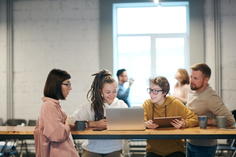 Coworkers around a table smiling and looking at a laptop